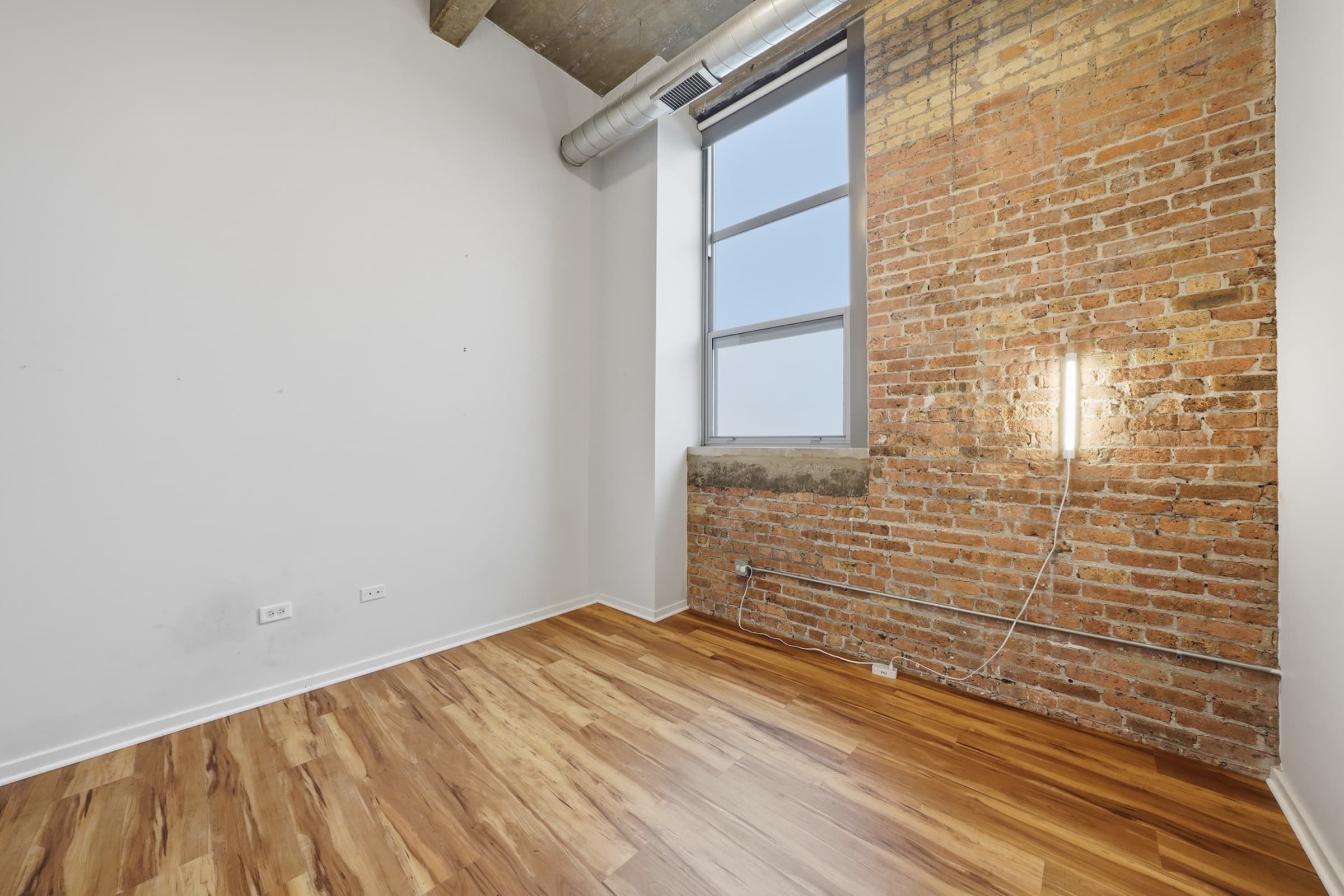 Second bedroom with exposed brick and a tall window