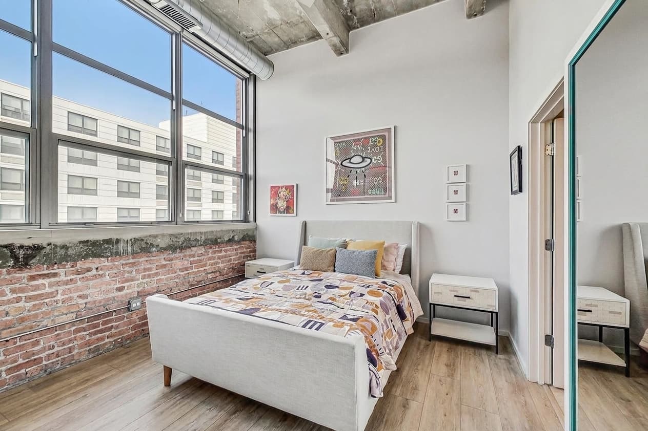 Bedroom one with exposed brick, tall window, and the new wide plank floors